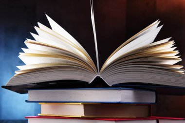 Bir yığın kitabın üzerinde açık bir kitap bulunan kompozisyon. 