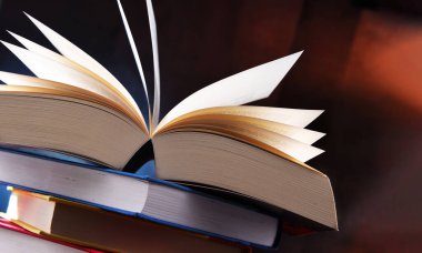 Bir yığın kitabın üzerinde açık bir kitap bulunan kompozisyon. 