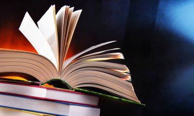 Bir yığın kitabın üzerinde açık bir kitap bulunan kompozisyon. 