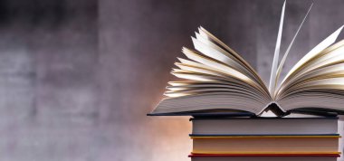 Bir yığın kitabın üzerinde açık bir kitap bulunan kompozisyon. 