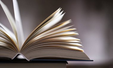 Bir yığın kitabın üzerinde açık bir kitap bulunan kompozisyon. 