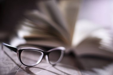 Gözlüklü kompozisyon ve masanın üzerinde açık kitap.