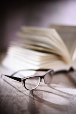 Gözlüklü kompozisyon ve masanın üzerinde açık kitap.