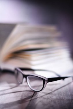 Gözlüklü kompozisyon ve masanın üzerinde açık kitap.