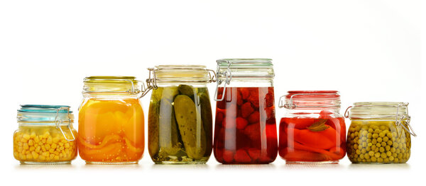 Jars with pickled vegetables and fruity compotes on white