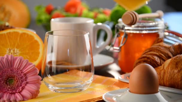 Llenado de vidrio con zumo de naranja en la mesa con desayuno — Vídeos de Stock