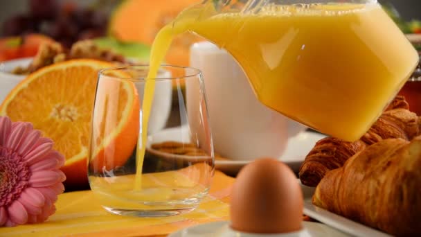 Llenado de vidrio con zumo de naranja en la mesa con desayuno — Vídeos de Stock