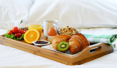 Otel odasında yatakta kahvaltı tepsisi.