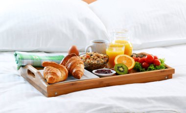 Otel odasında yatakta kahvaltı tepsisi.