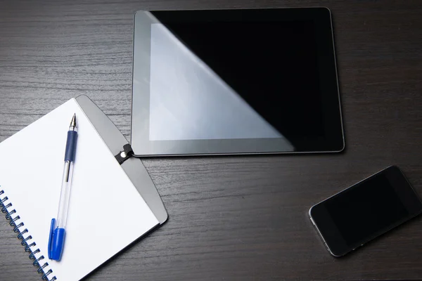 Tablet with phone and notepad on dark table — Stock Photo, Image
