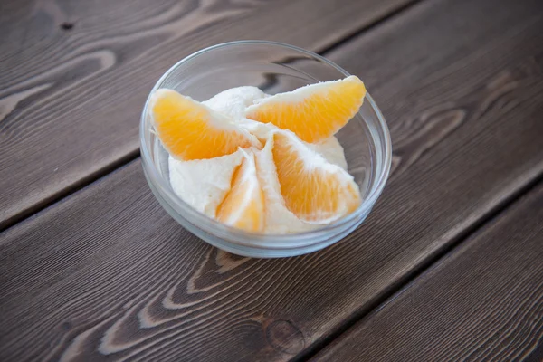 Iogurte e partes de laranja em um prato de vidro em uma mesa de madeira — Fotografia de Stock