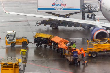 Rusya, Moskova, Sheremetyevo Havaalanı, 01.04.2021. Yükleyiciler havayolunun uçağından bavulları indiriyor. Sadece editörler kullanır. Servisler, yağmurlu havada havaalanında iş yaparlar..