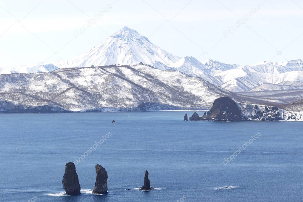 Russia, Kamchatka Peninsula. Three brothers rocks in the beautiful water of the bay and the Vilyuchinsky volcano in the background. Untouched nature of Russia. Suitable for postcards and advertising.