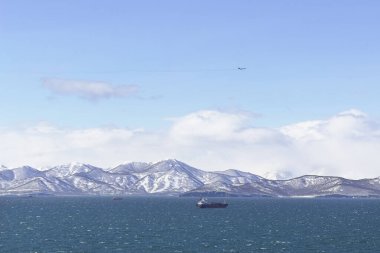 Russia, Kamchatka. Ships in the cold waters of the Avacha Bay. There are icy, snow-covered mountains and volcanoes in the background. clipart