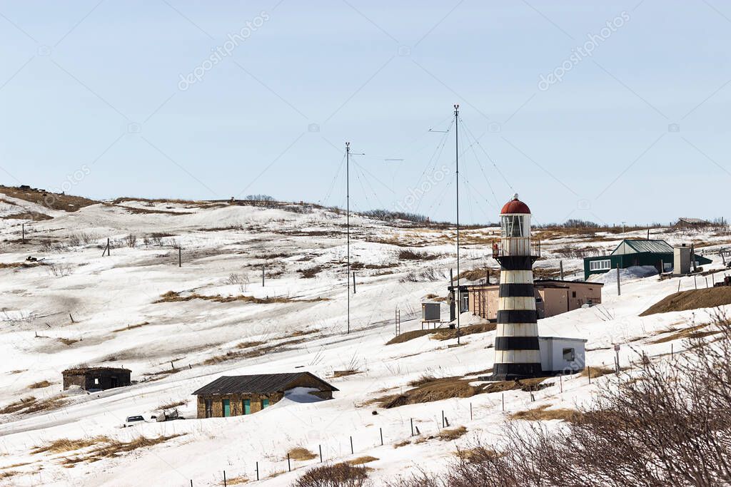 Petropavlovsky Lighthouse located on Mayachny Cape on Kamchatka Peninsula on shore of picturesque Avacha Gulf in the Pacific Ocean, in vicinity of Petropavlovsk-Kamchatsky City. Dirty melted snow.