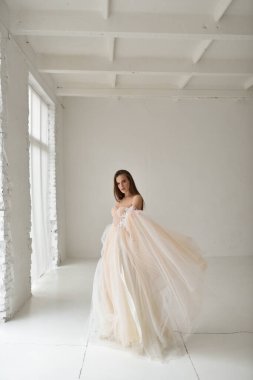 Gelinlik giymiş güzel bir gelin beyaz bir stüdyoda duruyor.