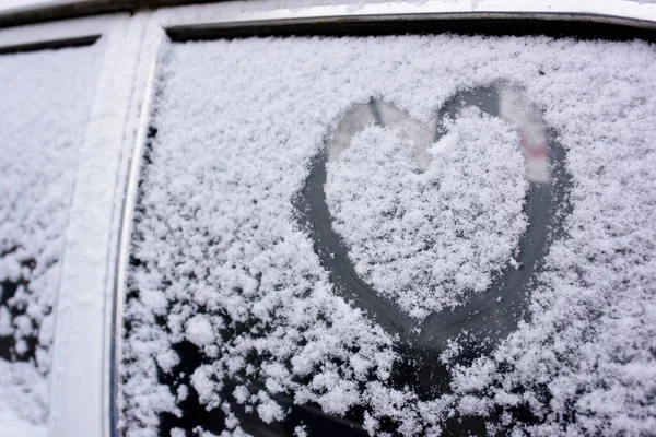 Heart drawn on a car windshield covered with fresh Christmas snow