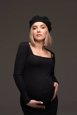 Siyah elbiseli güzel hamile kadın ellerini karnının üstüne koydu..