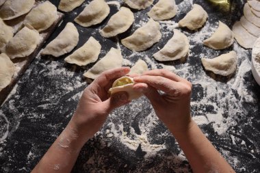 Kadın siyah arka planda el yapımı patatesle hamur köftesi heykeli yapıyor. Yukarıdan ateş edilmiş. Ukrayna halk mutfağı.
