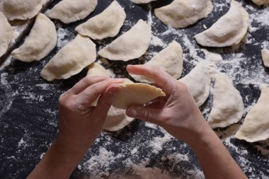 Kadın siyah arka planda el yapımı patatesle hamur köftesi heykeli yapıyor. Yukarıdan ateş edilmiş. Ukrayna halk mutfağı.