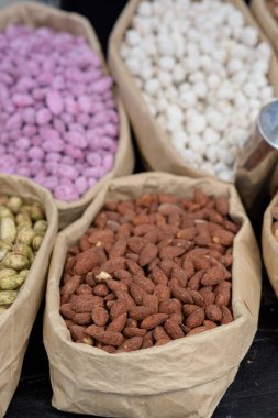 Badem ve baharatlı şam fıstığı tezgahın üzerinde kağıt torbalarda yatıyor..