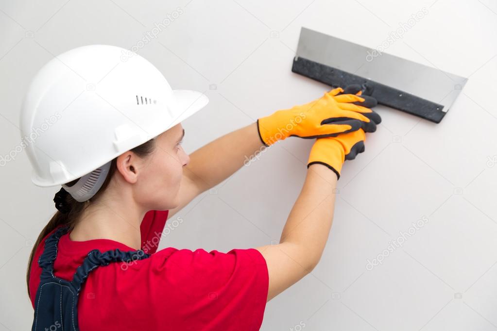 Female worker plastering wall with spatula tool