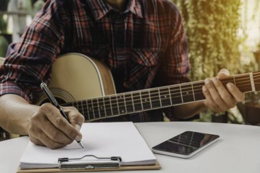 Şarkı yazmak için elinde kalem tutan bir şarkı yazarı. Akustik gitar çalan bir müzisyen. Canlı müzik ve soyut müzik konsepti.