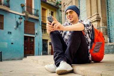 Yakışıklı delikanlı bir Avrupa şehri sokakta katta oturan smartphone kullanarak.