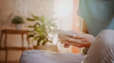 Güneşli bir günde Parlak Odada Zeminde oturan Akıllı Telefon Kullanan Kadın.