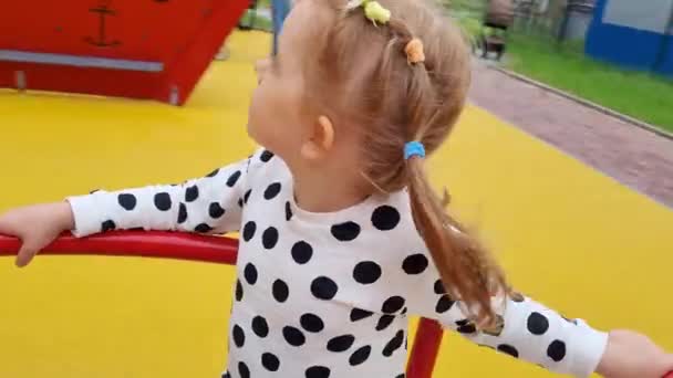 Chica feliz girando en tiovivo en un colorido parque infantil en el día de verano. — Vídeo de stock