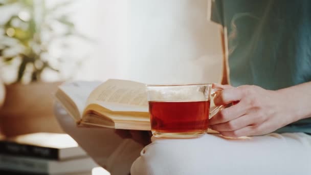 Femme tenant une tasse de thé ou de café fumant et lisant un livre. — Video