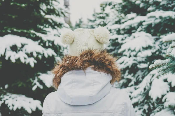 Jeune femme en bonnet tricoté va entre sapins dans une forêt . — Photo