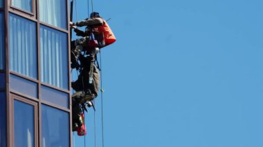 İki endüstriyel tırmanıcı bina üzerinde çalışıyor, camları onarıyor.