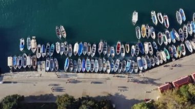 Havadan tepeden aşağı birçok tekne sete demirlemiş, tekneler rüzgarda savruluyor, insanlar deniz kenarındaki sokakta yürüyor, insanların güzel gölgeleri, görüntüye yakınlaşıyor..