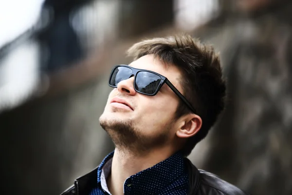 Junger schöner Mann steht mit Sonnenbrille gegen Wand — Stockfoto