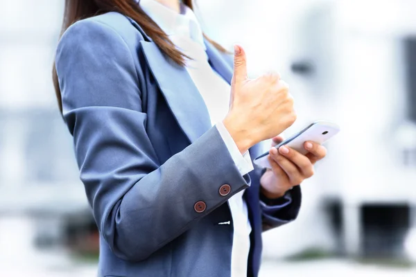 Красивая молодая бизнес-леди с помощью мобильного телефона на улице и знак ОК — стоковое фото