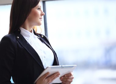 Havaalanında genç bir bayan yolcu, uçağını beklerken tablet bilgisayarını kullanıyor.