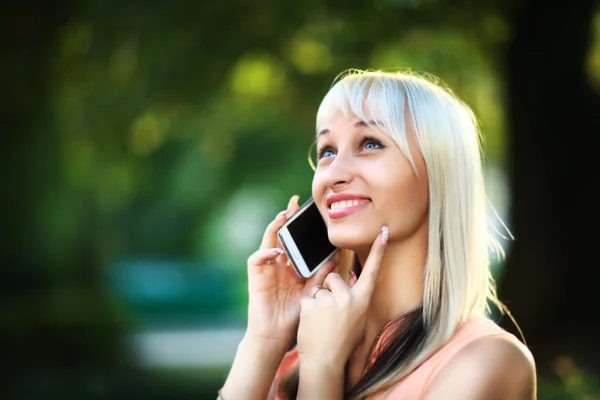 Portret van een mooie vrouw die typt op de smartphone in een park met een groene achtergrond — Stockfoto