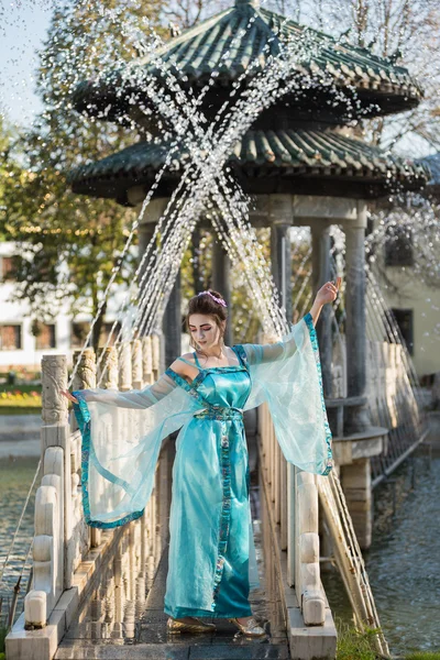 Красивая молодая гейша в каплях в голубом платье, стоящая у фонтана — стоковое фото