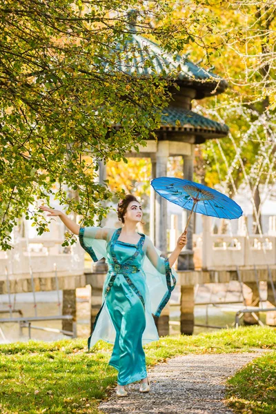 Beautiful geisha with a blue umbrella near green apple tree — Stock Photo, Image