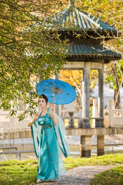 Beautiful geisha with a blue umbrella near green apple tree — Stock Photo, Image