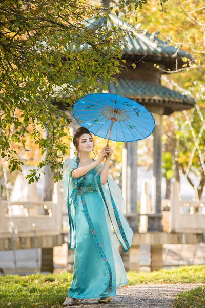 Bela gueixa com um guarda-chuva azul perto de árvore de maçã verde — Fotografia de Stock