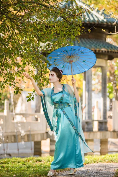 Bela gueixa com um guarda-chuva azul perto de árvore de maçã verde — Fotografia de Stock