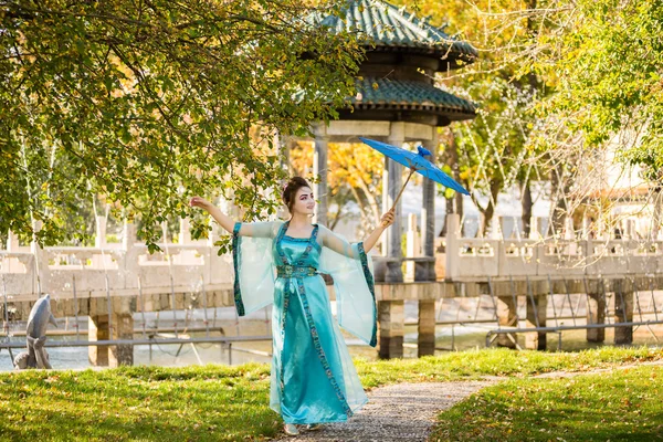 Beautiful geisha with a blue umbrella near green apple tree — Stock Photo, Image