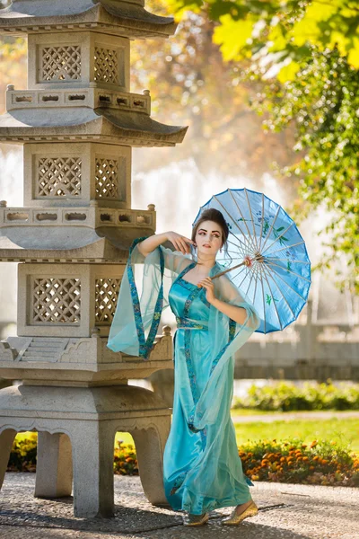 Bela gueixa com um guarda-chuva azul perto de pedra pagode — Fotografia de Stock