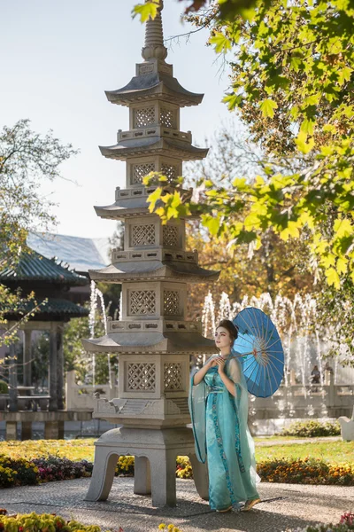 Beautiful geisha with a blue umbrella near stone pagoda — Stock Photo, Image