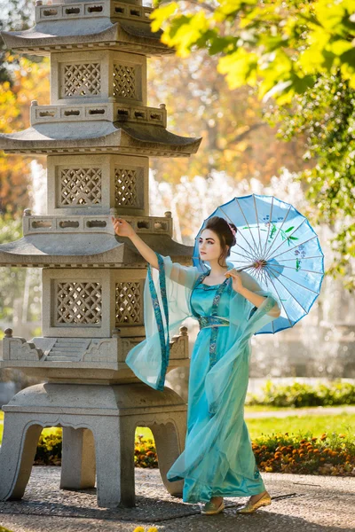 Beautiful geisha with a blue umbrella near stone pagoda — Stock Photo, Image