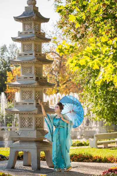 Beautiful geisha with a blue umbrella near stone pagoda — Stock Photo, Image