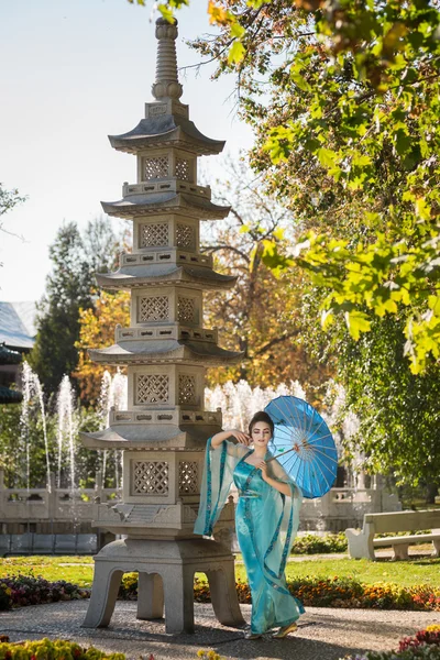 Bela gueixa com um guarda-chuva azul perto de pedra pagode — Fotografia de Stock