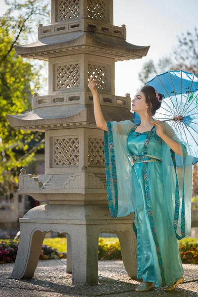 Beautiful geisha with a blue umbrella near stone pagoda — Stock Photo, Image